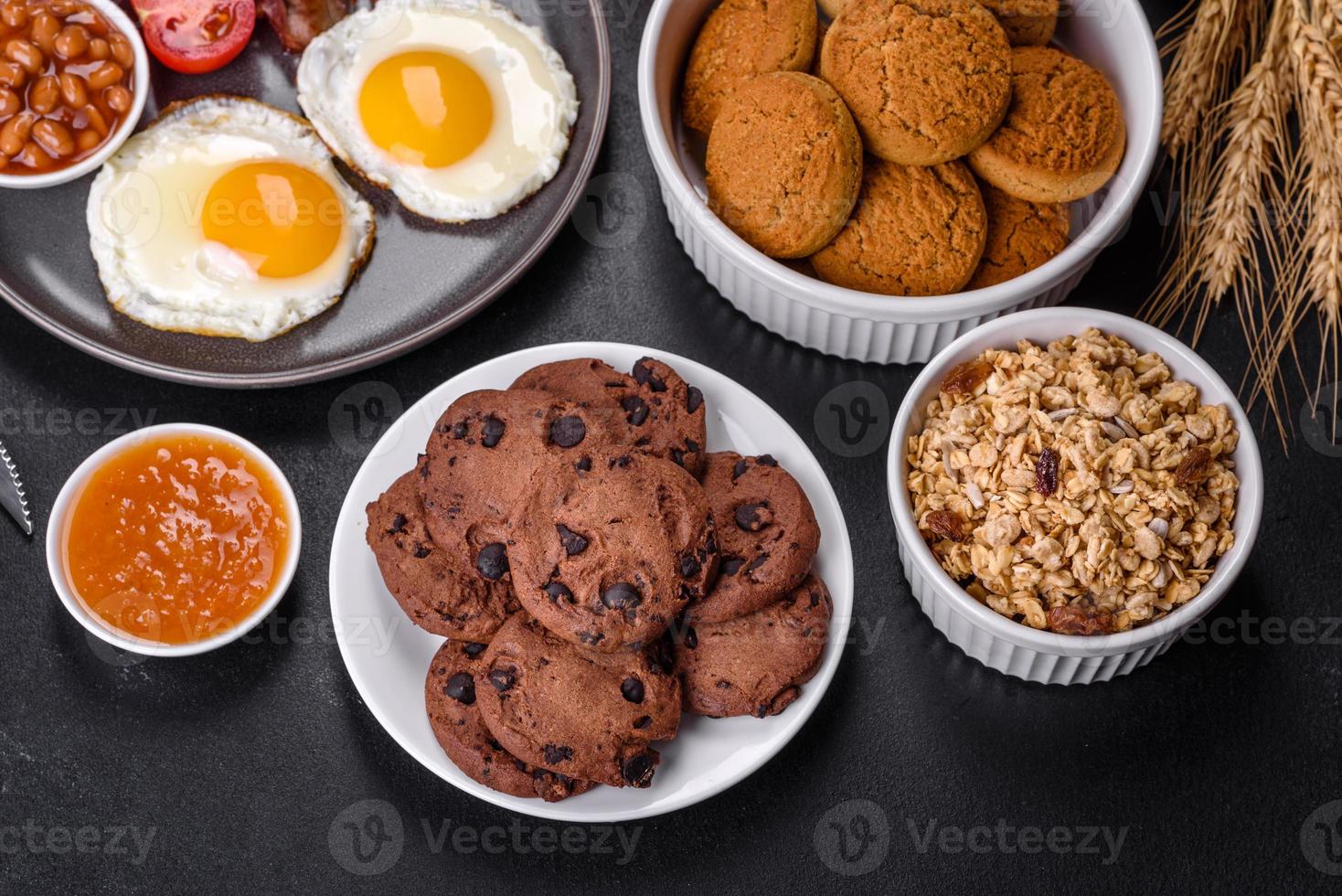 A delicious nutritious healthy breakfast with fried eggs, bacon, beans, a glass of juice, oat cookies, milk and jam photo