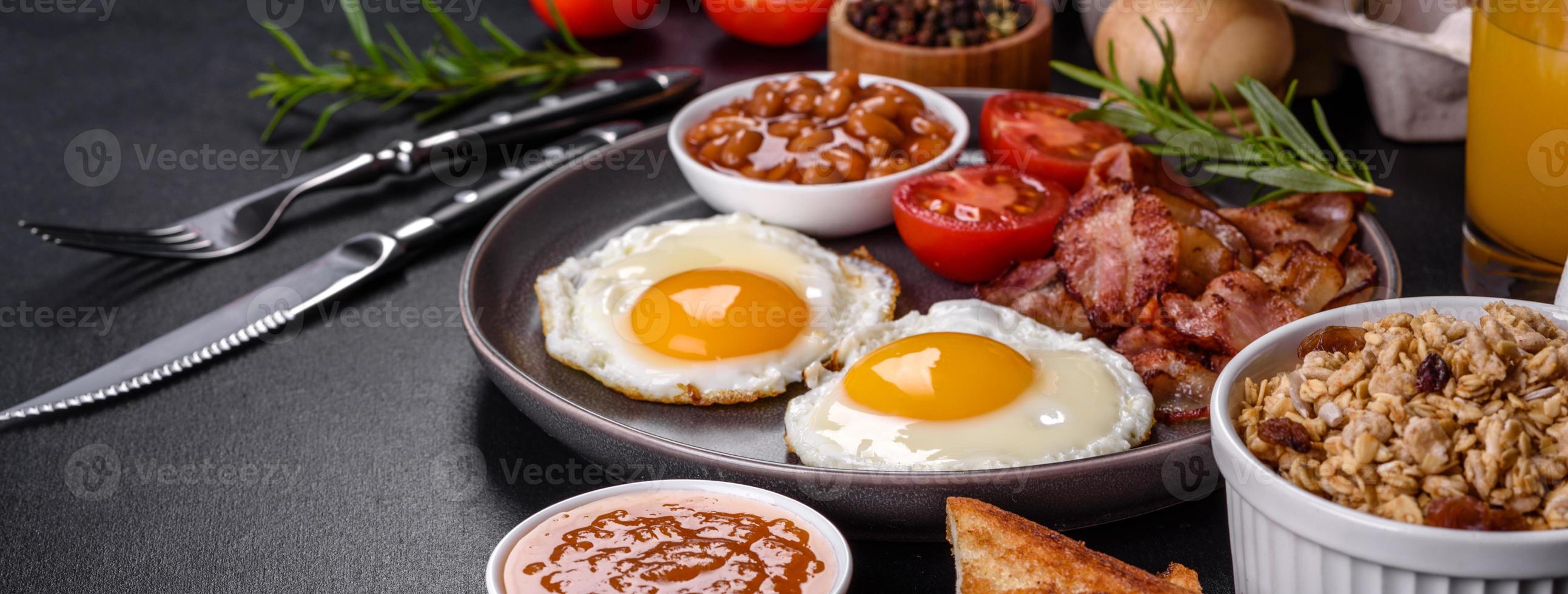 A delicious nutritious healthy breakfast with fried eggs, bacon, beans, a glass of juice, oat cookies, milk and jam photo