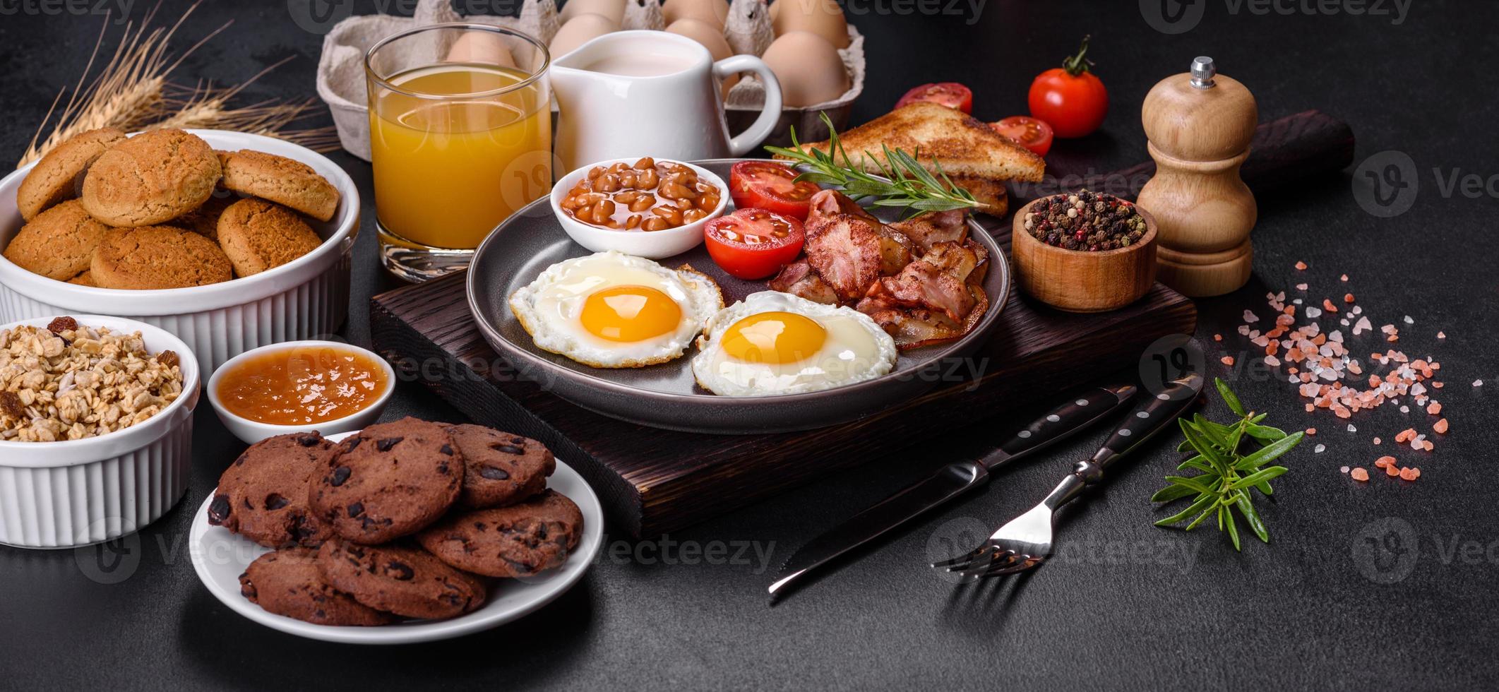A delicious nutritious healthy breakfast with fried eggs, bacon, beans, a glass of juice, oat cookies, milk and jam photo