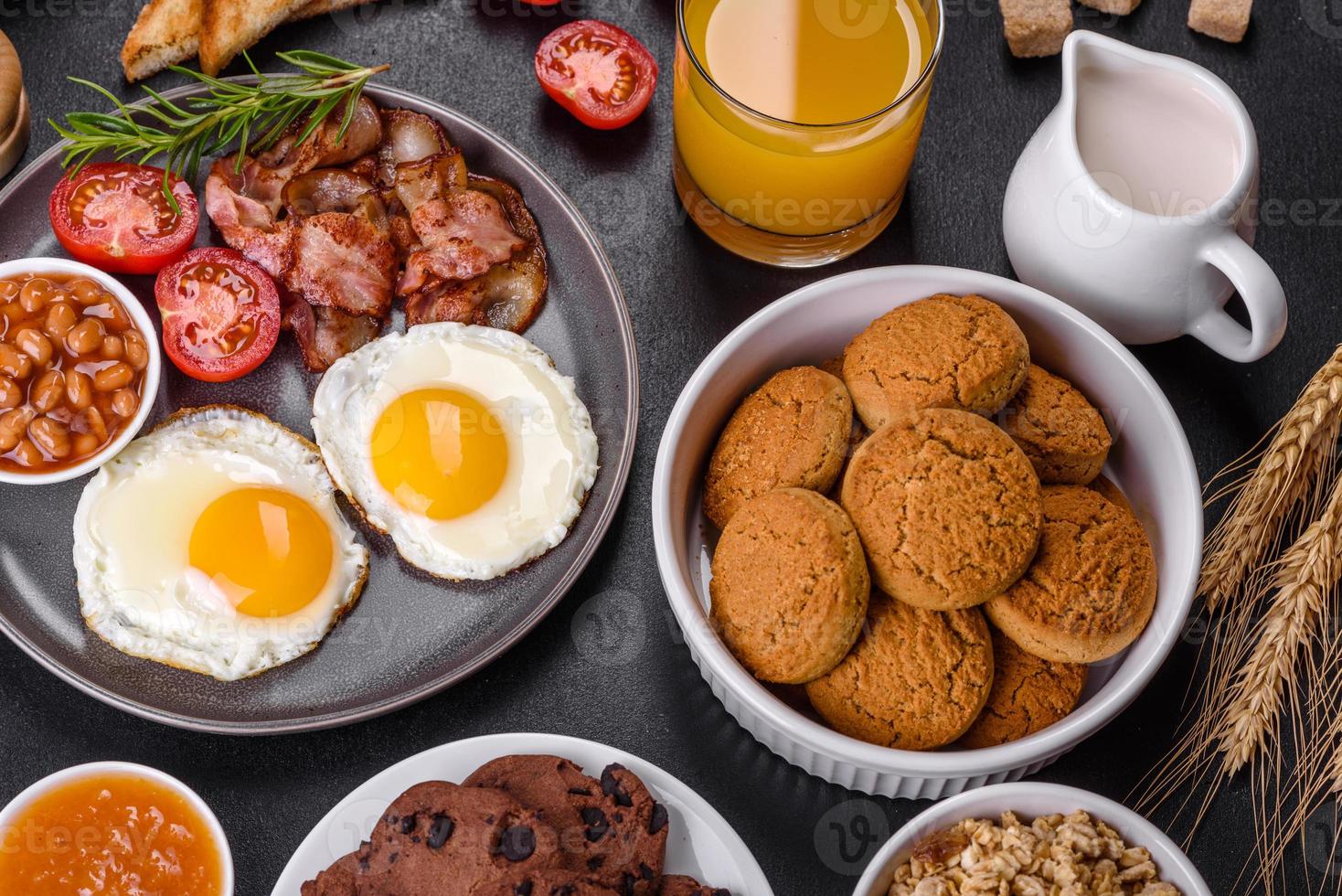 A delicious nutritious healthy breakfast with fried eggs, bacon, beans, a glass of juice, oat cookies, milk and jam photo