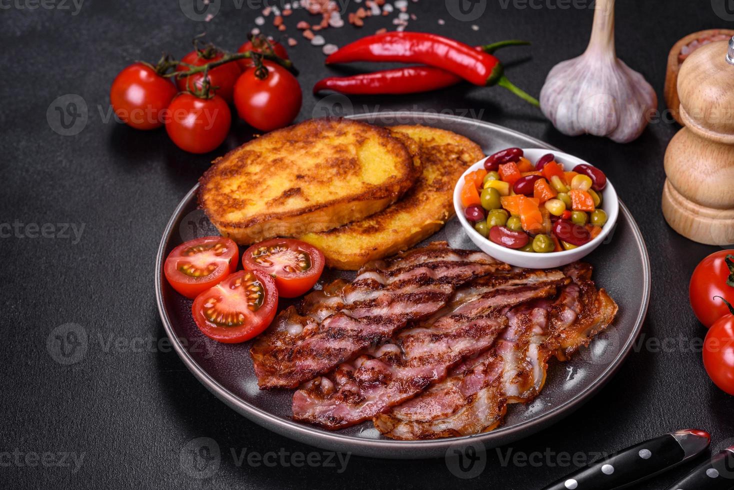 Slices of delicious grilled bacon with croutons fried in egg with spices, salt, vegetables and herbs photo