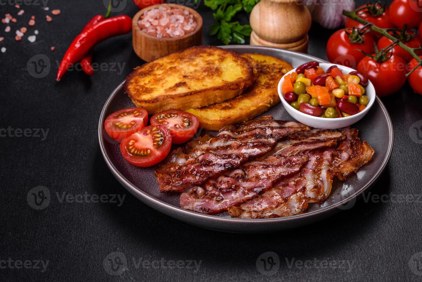 Slices of delicious grilled bacon with croutons fried in egg with spices, salt, vegetables and herbs photo