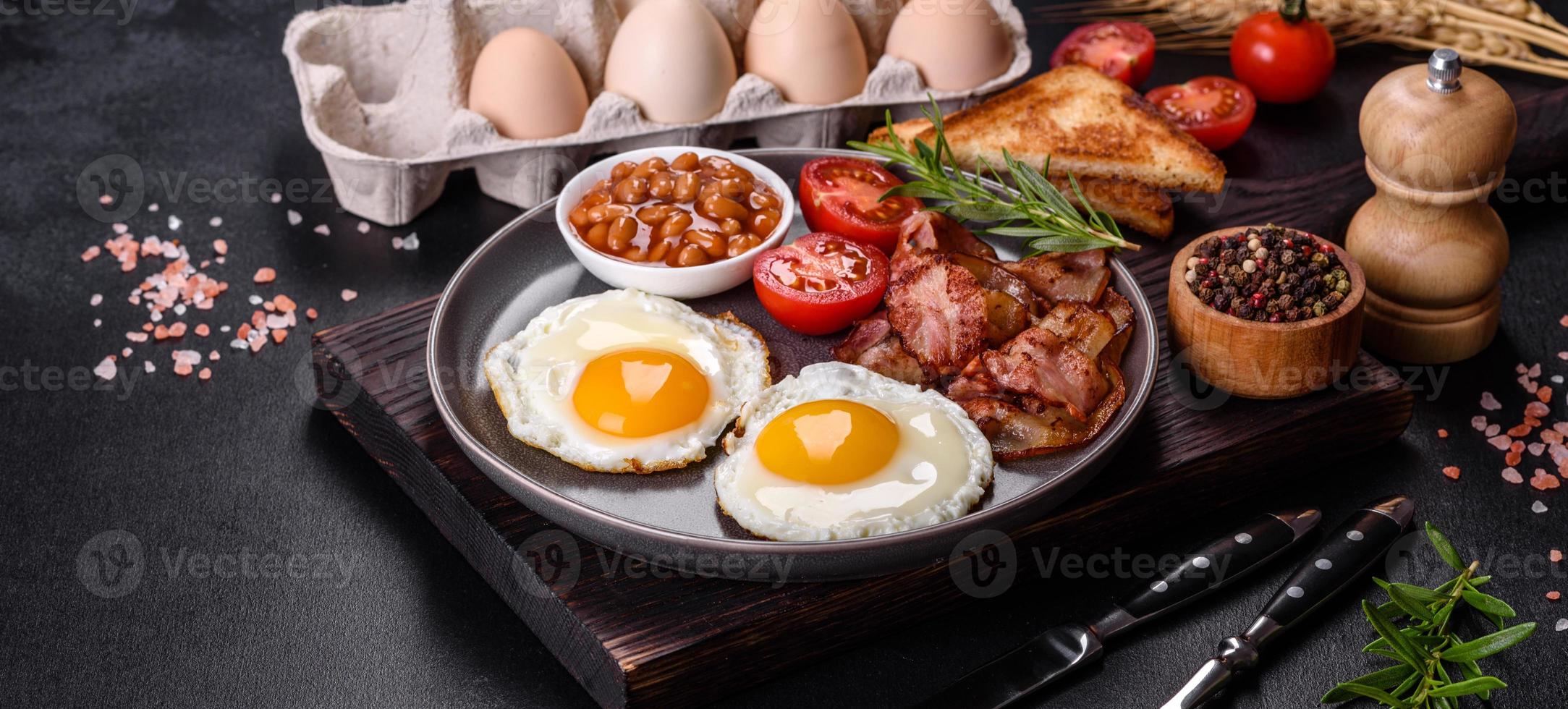 A delicious nutritious healthy breakfast with fried eggs, bacon, beans, a glass of juice, oat cookies, milk and jam photo