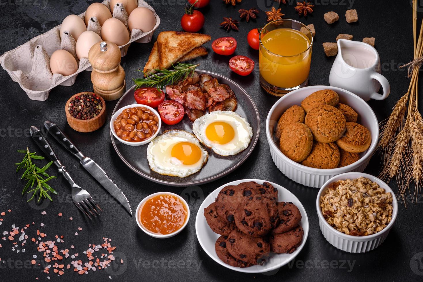 A delicious nutritious healthy breakfast with fried eggs, bacon, beans, a glass of juice, oat cookies, milk and jam photo