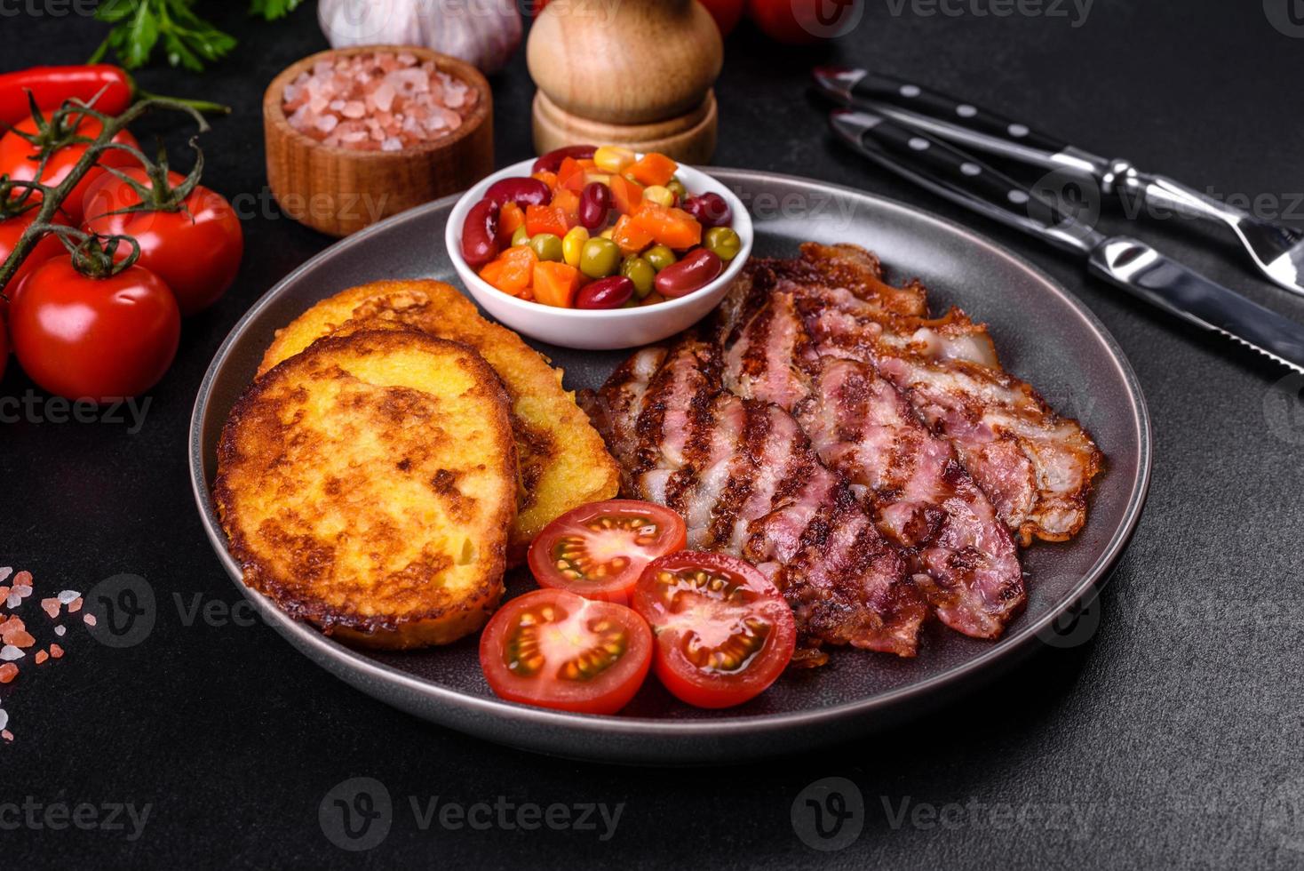 Slices of delicious grilled bacon with croutons fried in egg with spices, salt, vegetables and herbs photo