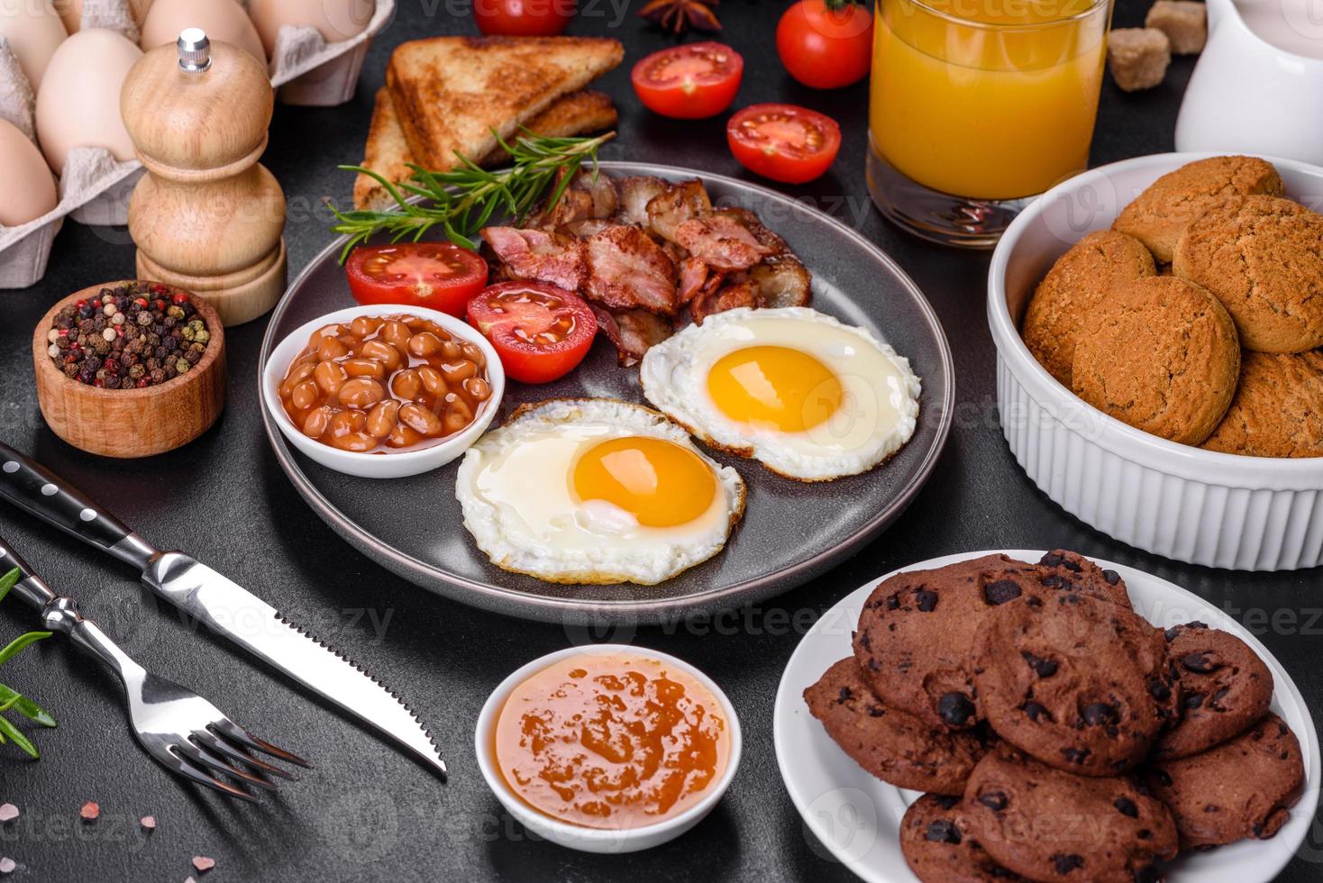 un delicioso desayuno saludable y nutritivo con huevos fritos, tocino, frijoles, un vaso de jugo, galletas de avena, leche y mermelada foto