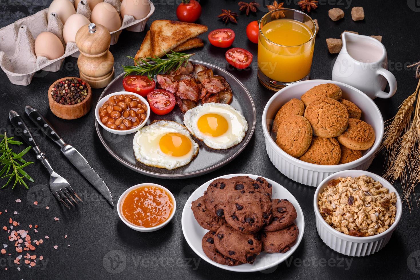 A delicious nutritious healthy breakfast with fried eggs, bacon, beans, a glass of juice, oat cookies, milk and jam photo