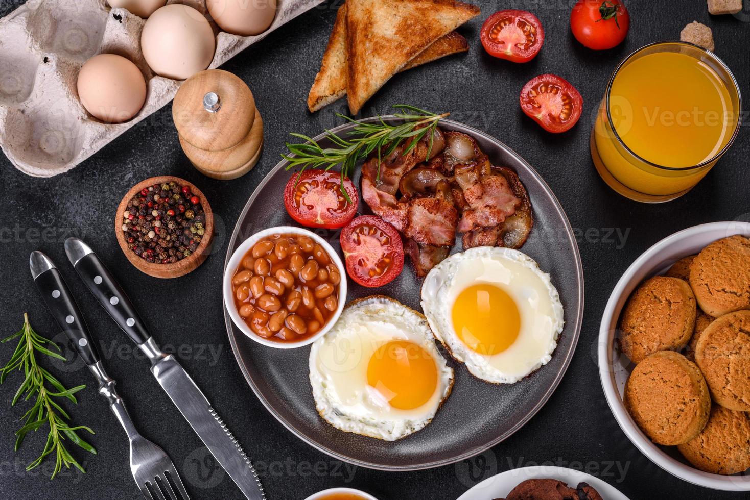 A delicious nutritious healthy breakfast with fried eggs, bacon, beans, a glass of juice, oat cookies, milk and jam photo