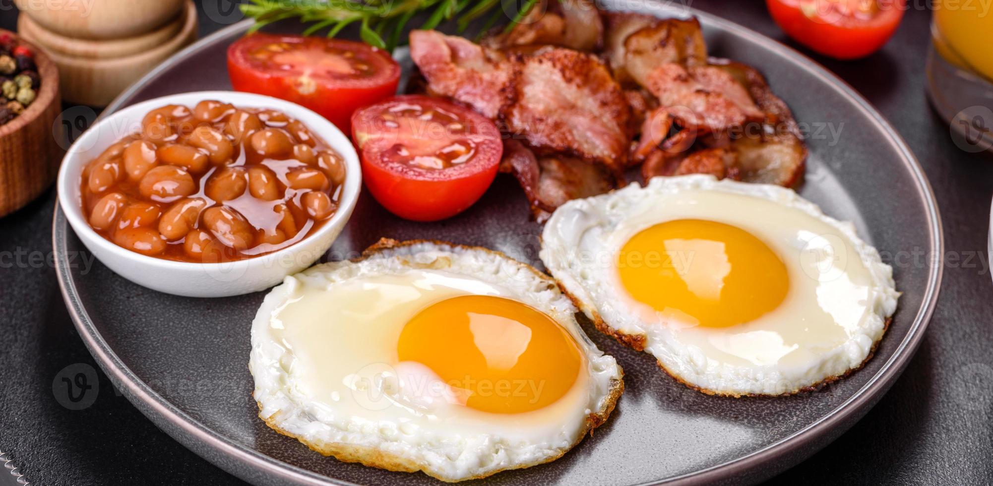A delicious nutritious healthy breakfast with fried eggs, bacon, beans, a glass of juice, oat cookies, milk and jam photo