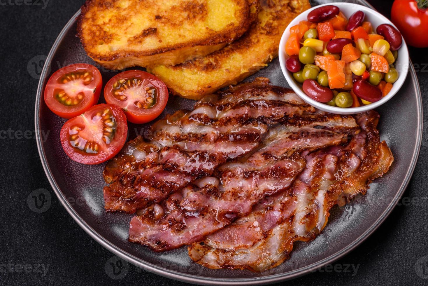 Slices of delicious grilled bacon with croutons fried in egg with spices, salt, vegetables and herbs photo