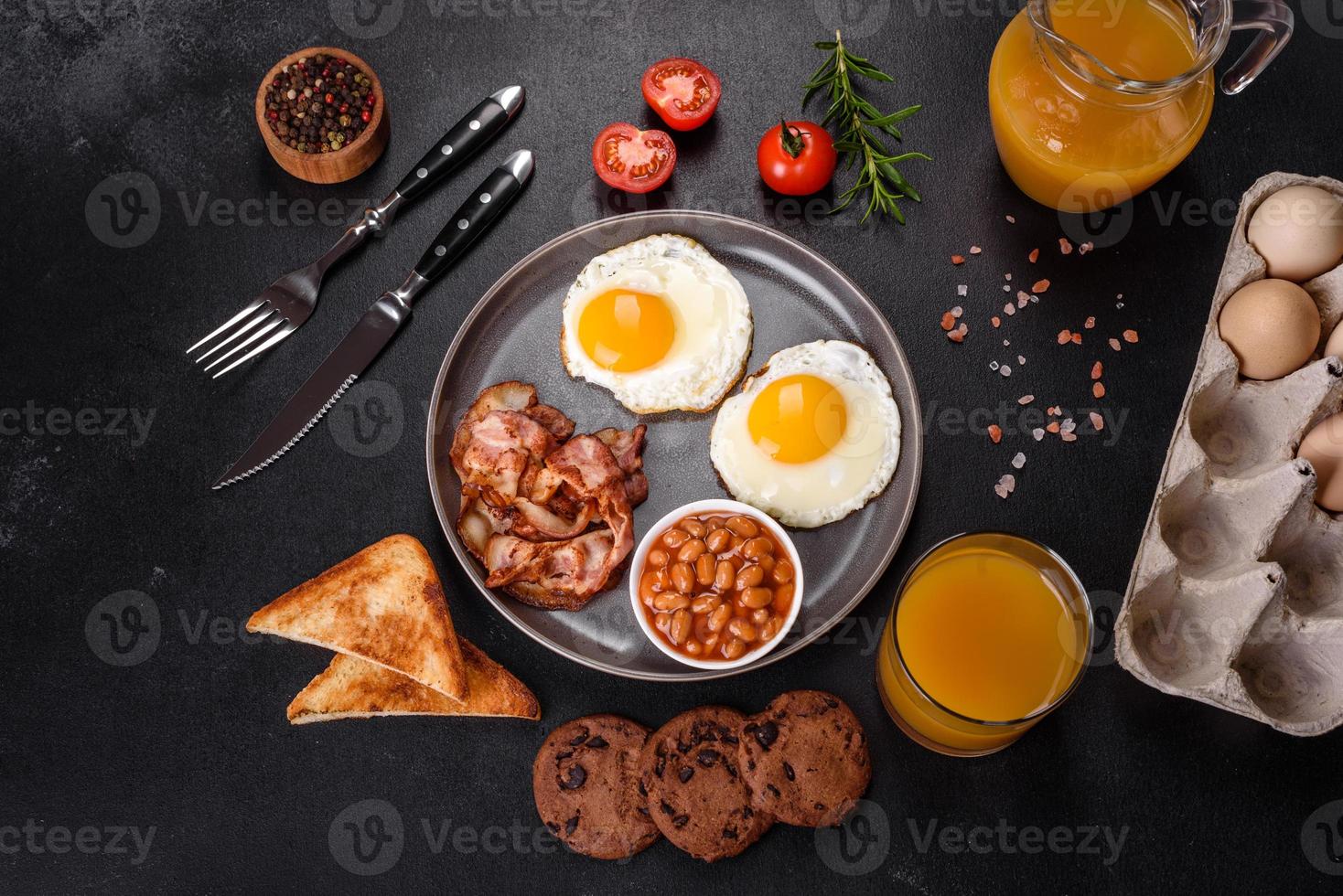 A delicious nutritious healthy breakfast with fried eggs, bacon, beans, a glass of juice, oat cookies, milk and jam photo