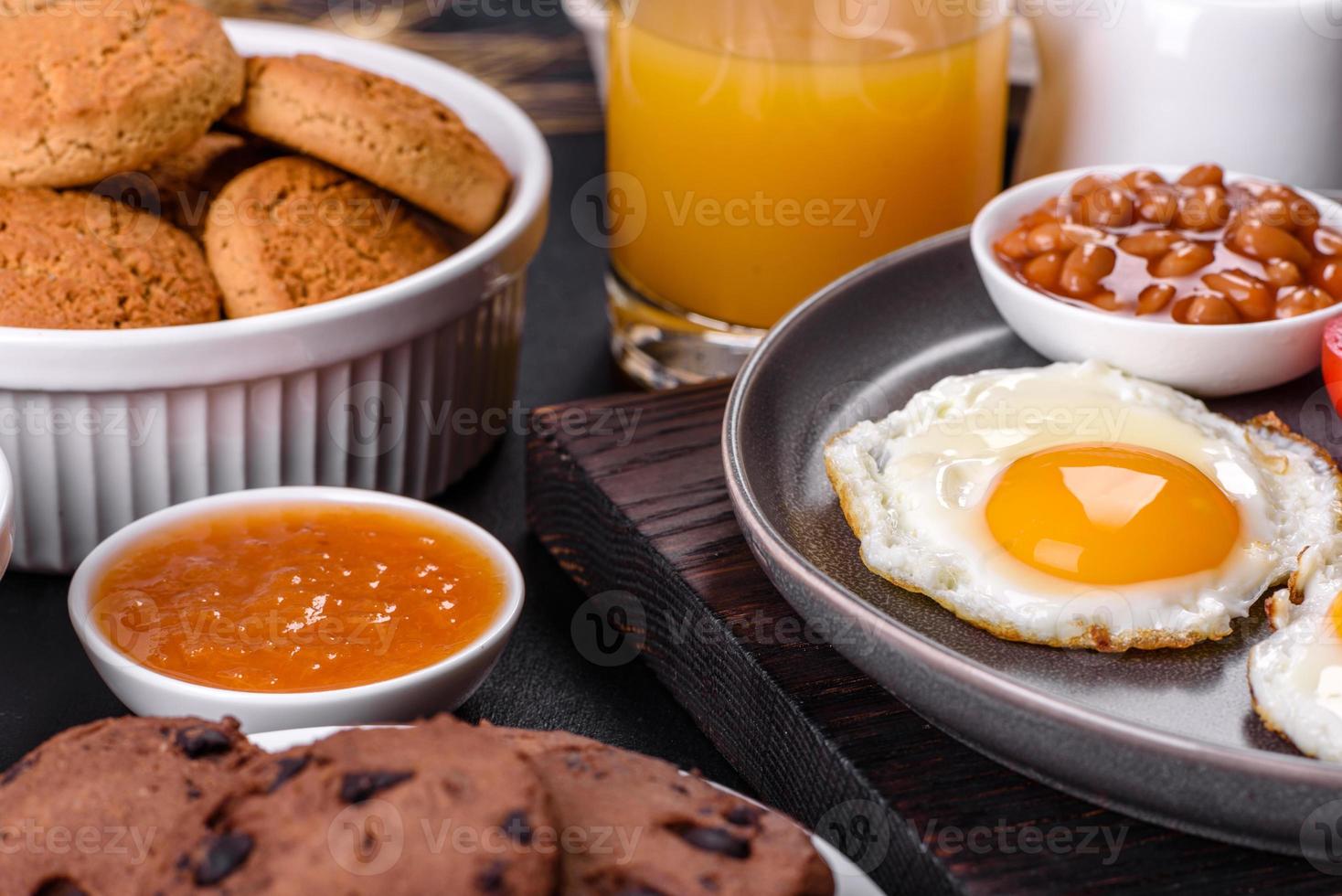 A delicious nutritious healthy breakfast with fried eggs, bacon, beans, a glass of juice, oat cookies, milk and jam photo