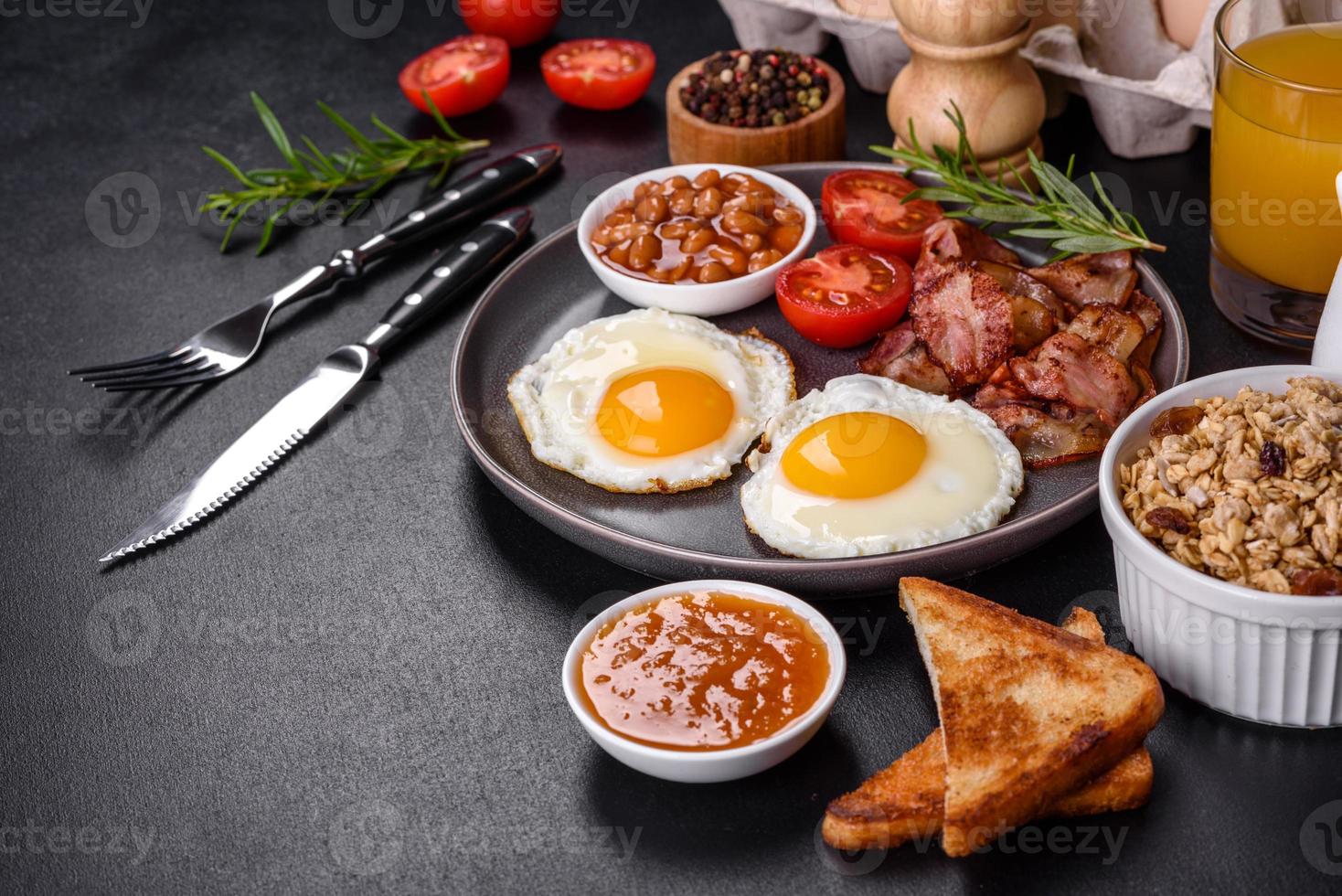 un delicioso desayuno saludable y nutritivo con huevos fritos, tocino, frijoles, un vaso de jugo, galletas de avena, leche y mermelada foto