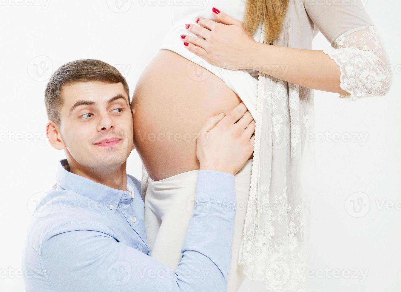 Handsome man is listening to his beautiful pregnant wife's tummy and smiling photo