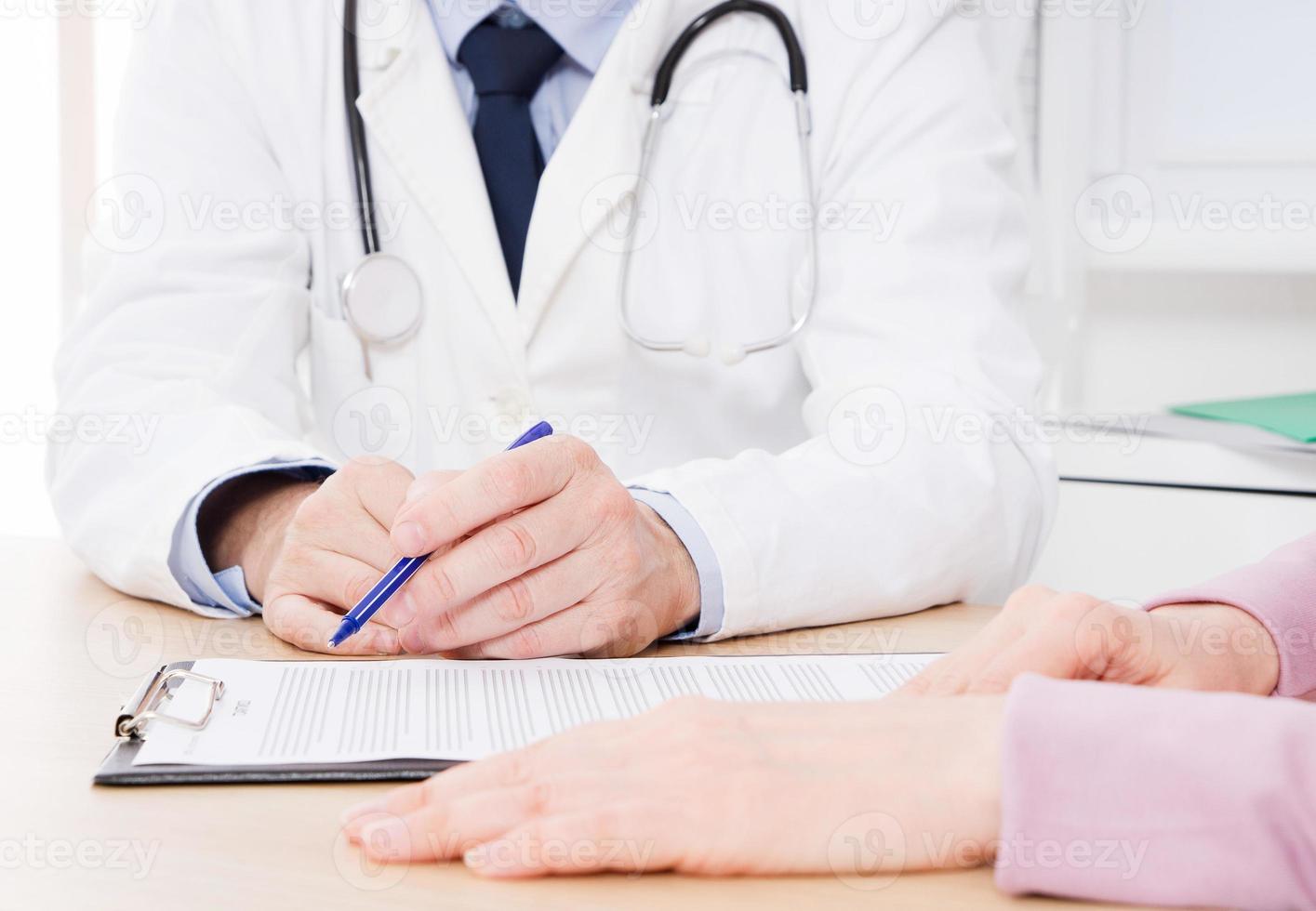Patient listening intently to a male doctor explaining patient symptoms or asking a question as they discuss paperwork together in a consultation photo