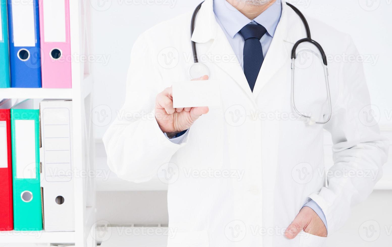 doctor in hospital hold business card, medical insurance, man in white uniform. Copy space photo