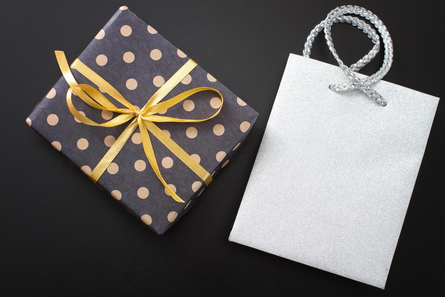 Gift box in polka dots and paper bag on black background. Top view and copy space photo