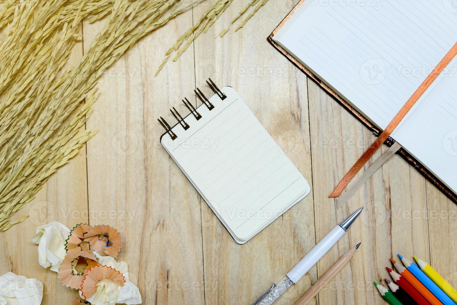 Small note book paper or notepad for writing information with pen, color pencil, pencil, book and crumpled paper balls on wooden table. view from above photo