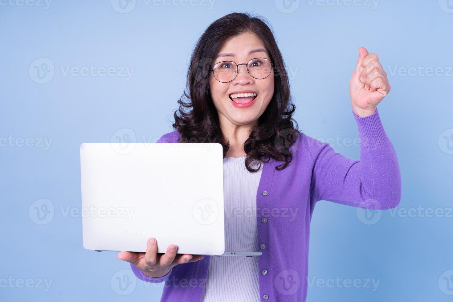 Portrait of middle aged Asian woman using laptop on blue background photo