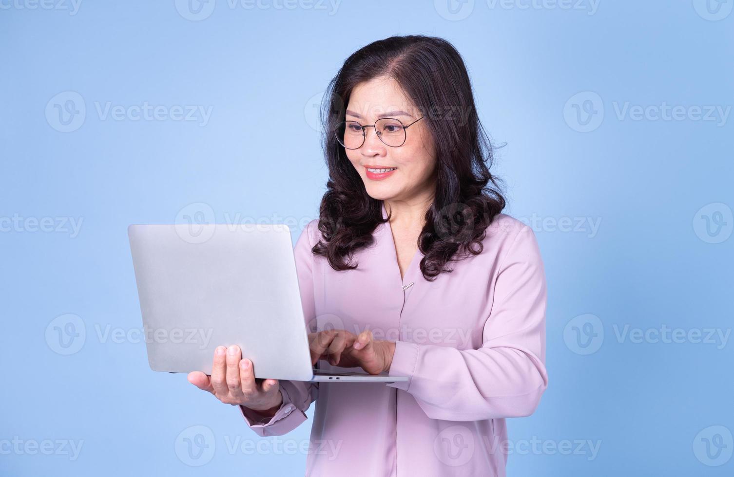 Portrait of middle aged Asian woman using laptop on blue background photo