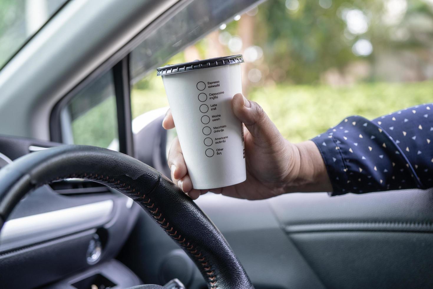 Señora asiática que sostiene la comida caliente de la taza de café para beber en el coche, peligrosa y con riesgo de accidente. foto