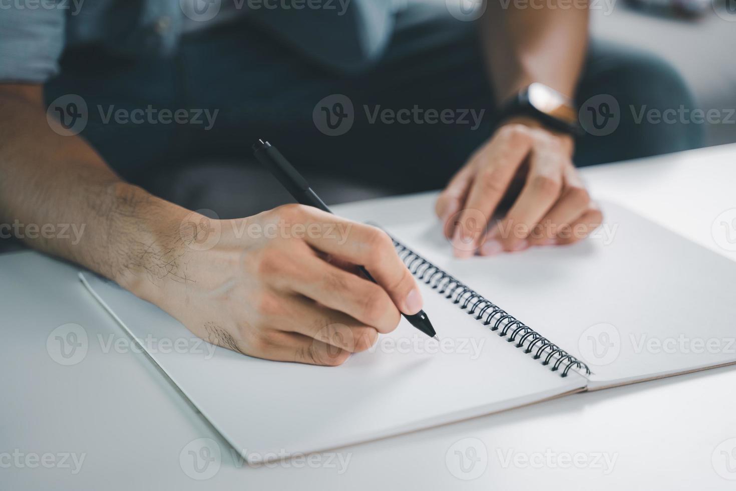 Cerca de joven en manos de tela casual escribiendo en el bloc de notas, cuaderno con bolígrafo sobre la mesa. foto