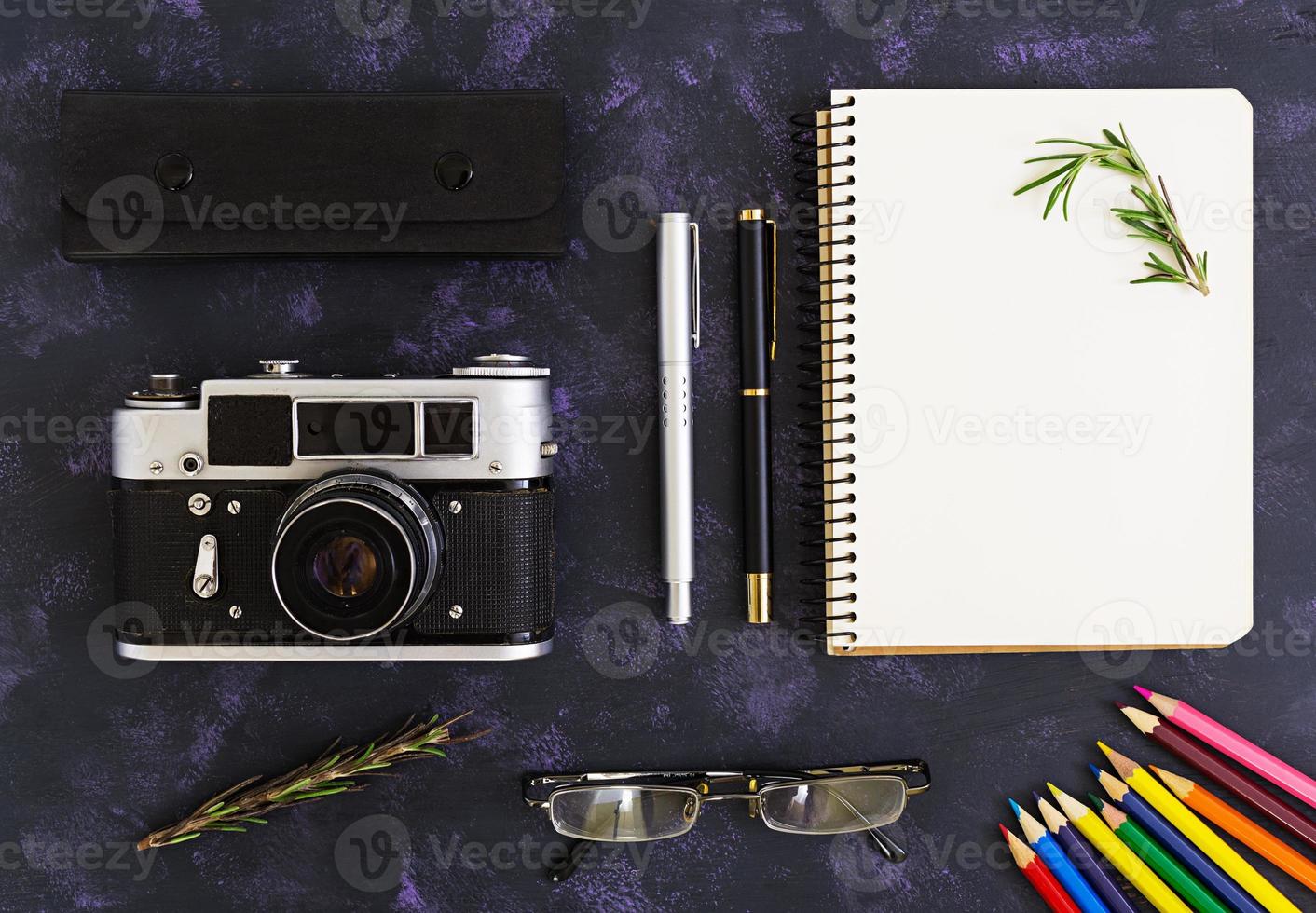Flat lay, top view office table desk. Desk workspace with retro camera, diary, pen, glasses, case, rosemary on dark background. photo
