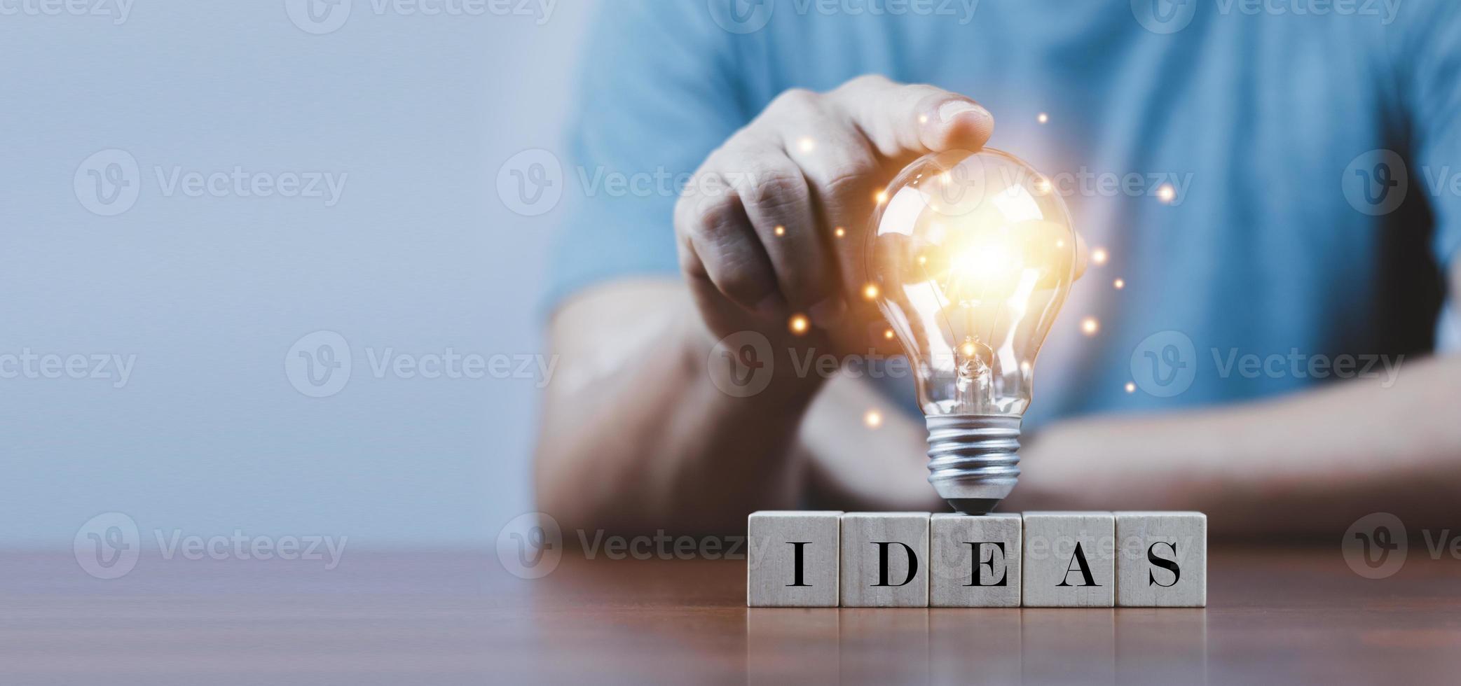 mano tocando una bombilla en un bloque de madera con ideas de palabras, nuevo concepto de idea con innovación e inspiración, tecnología innovadora en el concepto de ciencia y comunicación. foto