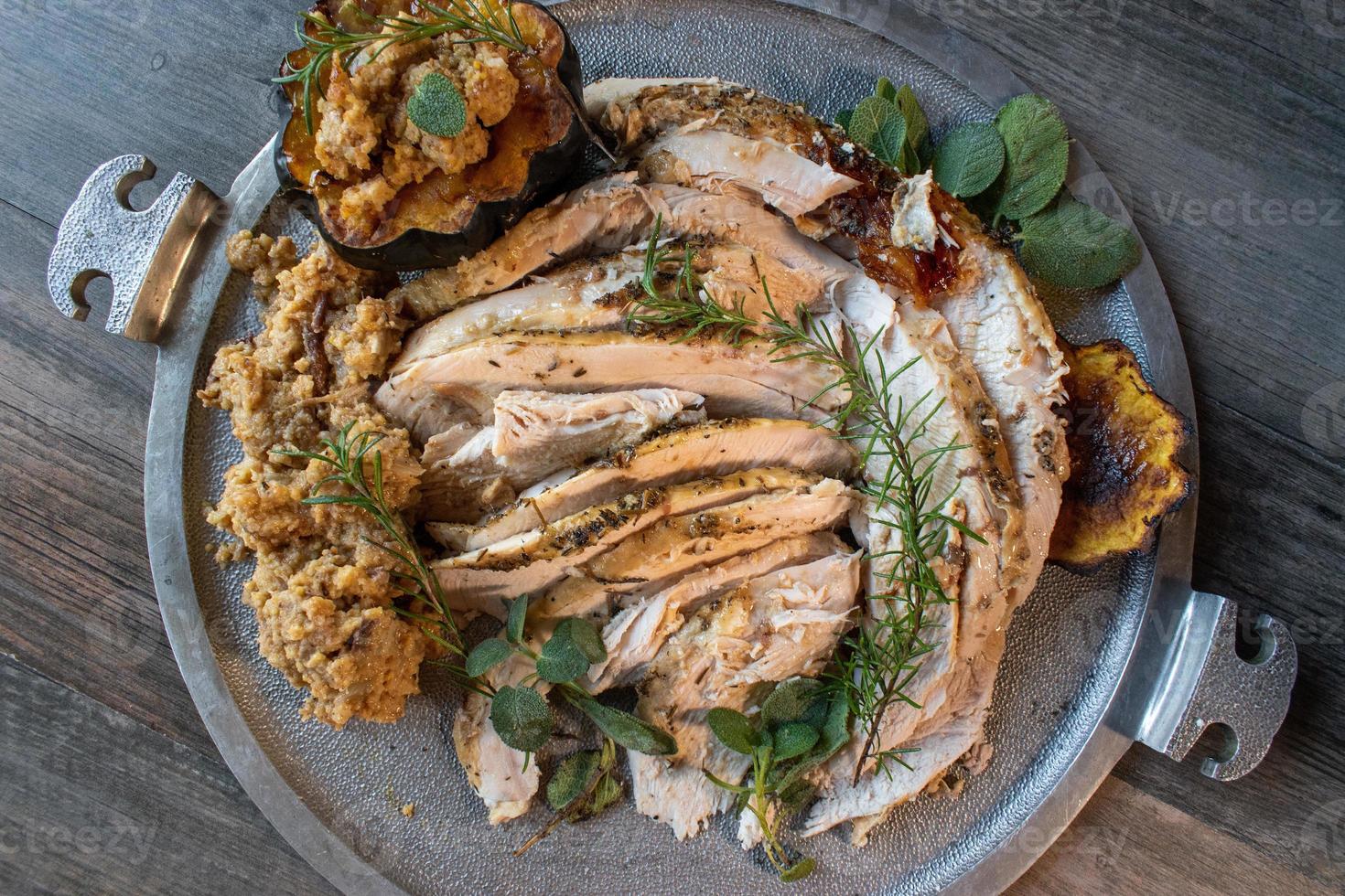 Serving tray of sliced roasted turkey with Thanksgiving sides and garnished with rosemary and sage photo
