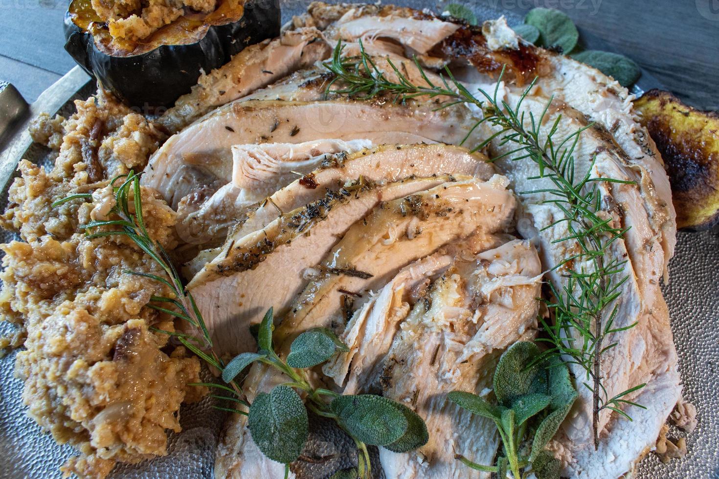 Serving tray of sliced roasted turkey with Thanksgiving sides and garnished with rosemary and sage photo