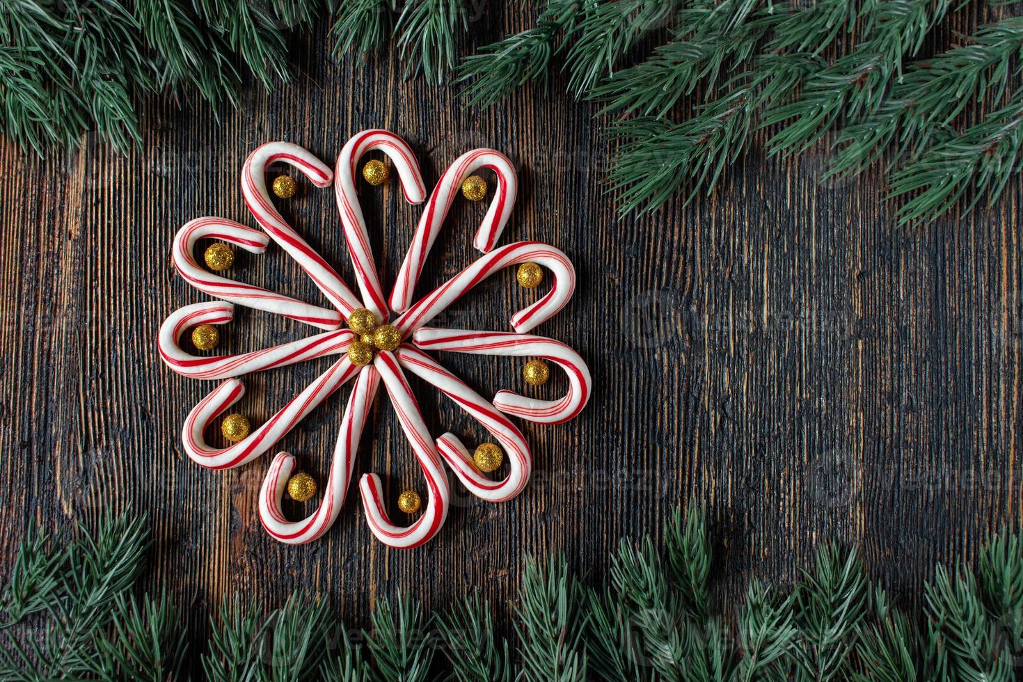 bastones de caramelo en un diseño de flores con bolas de oro brillante con borde de árbol verde con espacio de copia plano foto