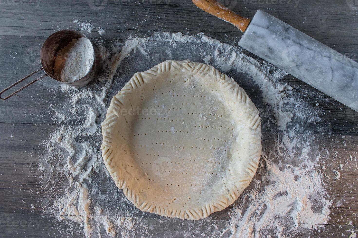Making rustic pastry dough pie shell on floured surface with rolling pin flat lay photo