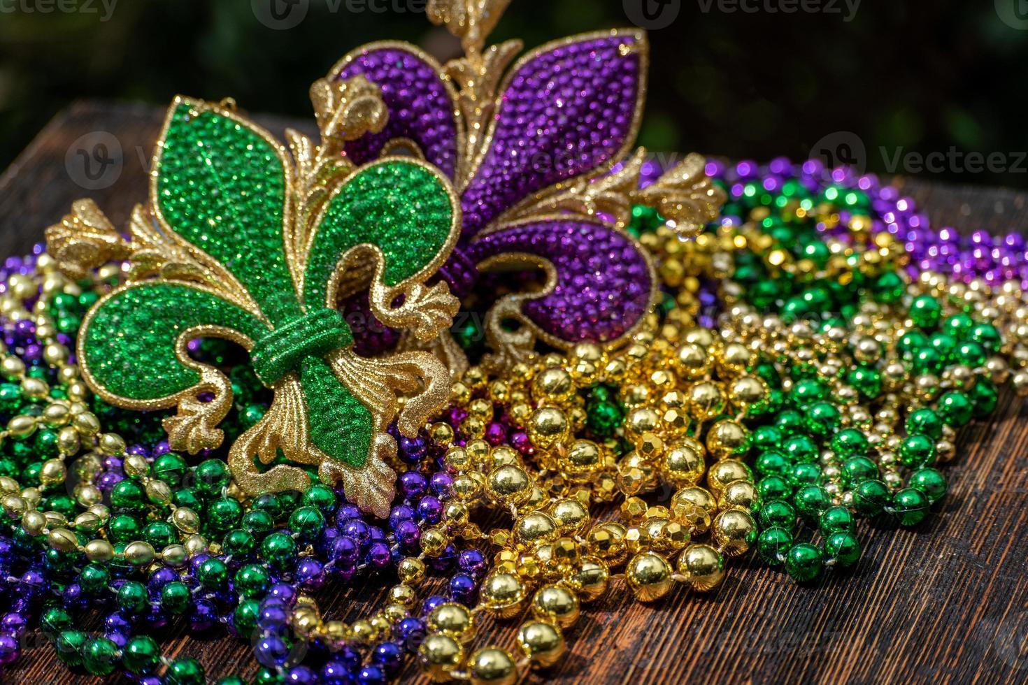 Mardi Gras color beads with fleur de lis on wooden table in sunlight photo