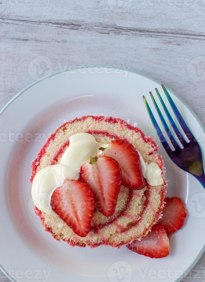 Serving of jelly roll cake slice with cream and fresh strawberry slices on plate flat lay photo