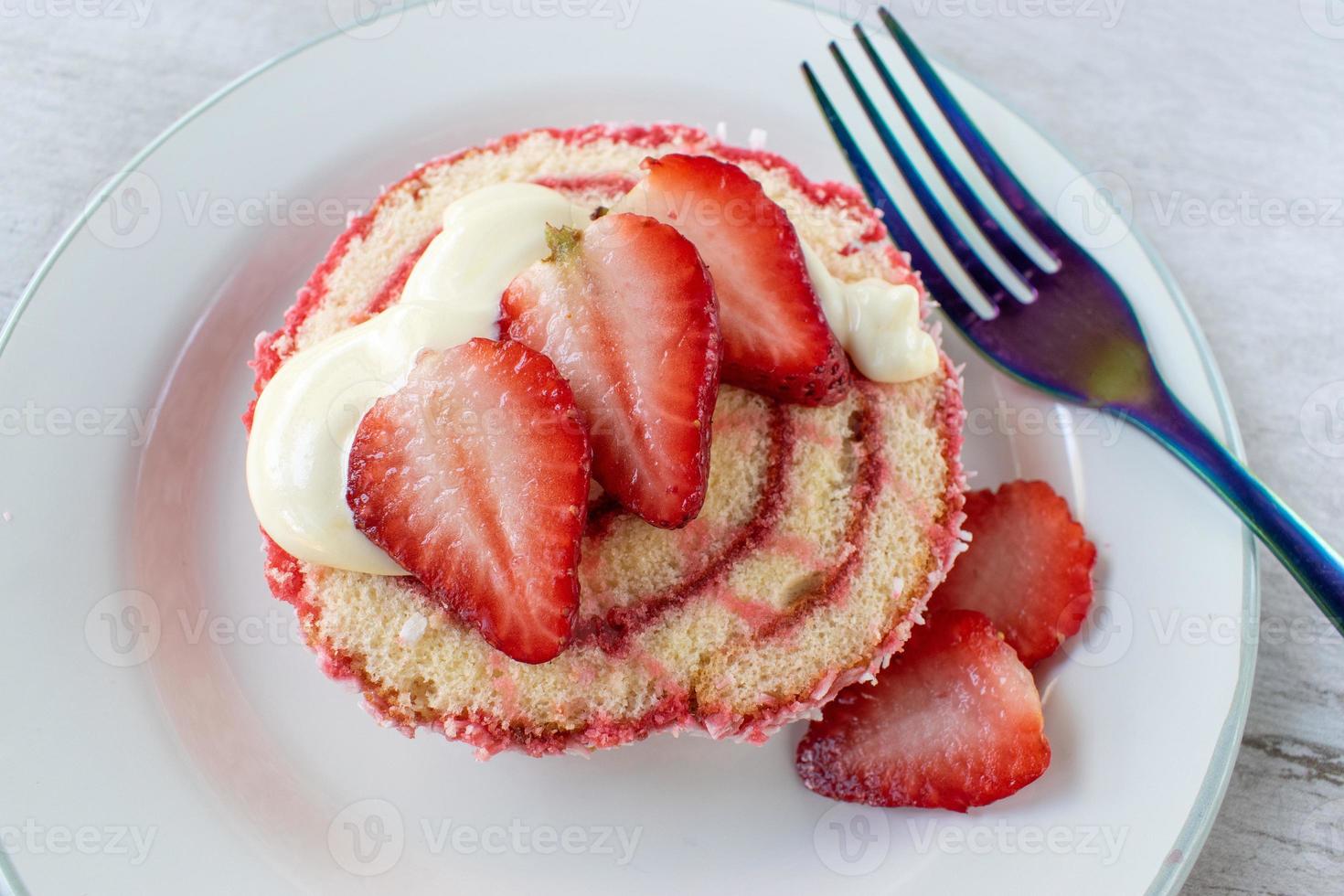 Serving of jelly roll cake slice with cream and fresh strawberry slices on plate flat lay photo