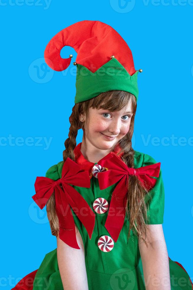 niña sonriente vestida como duende navideño con fondo de pantalla azul foto