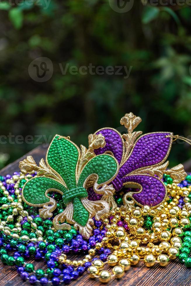 Mardi Gras color beads with fleur de lis on wooden table in sunlight photo