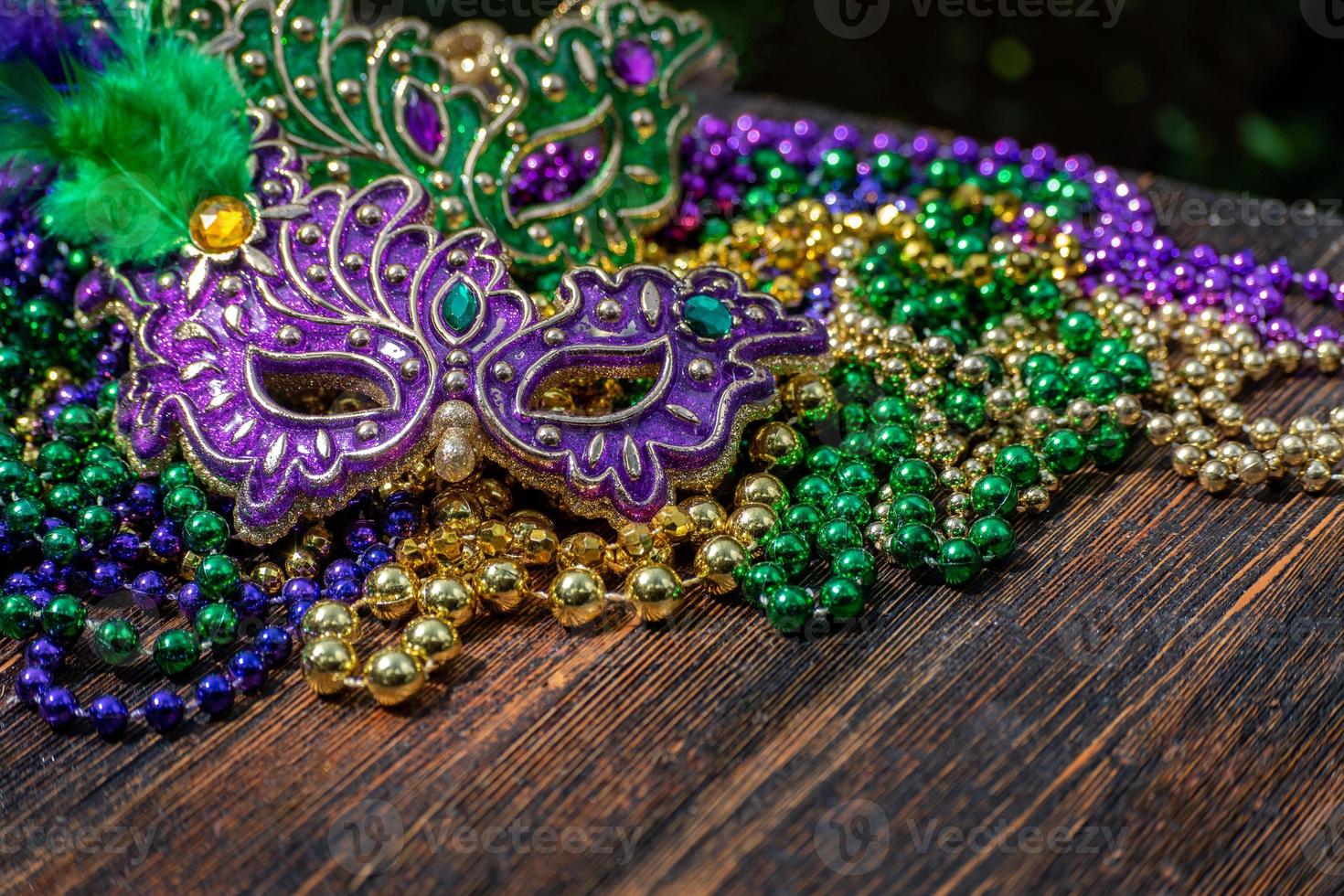 Mardi Gras color beads with masks on wooden table in sunlight photo