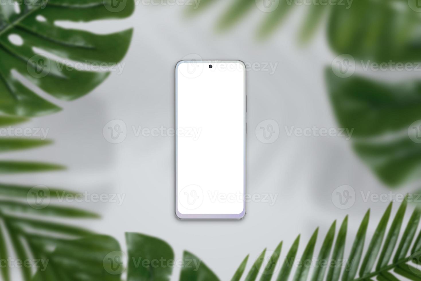 Phone mockup on gray surface surrounded by green leafs. Top view, flat lay composition photo