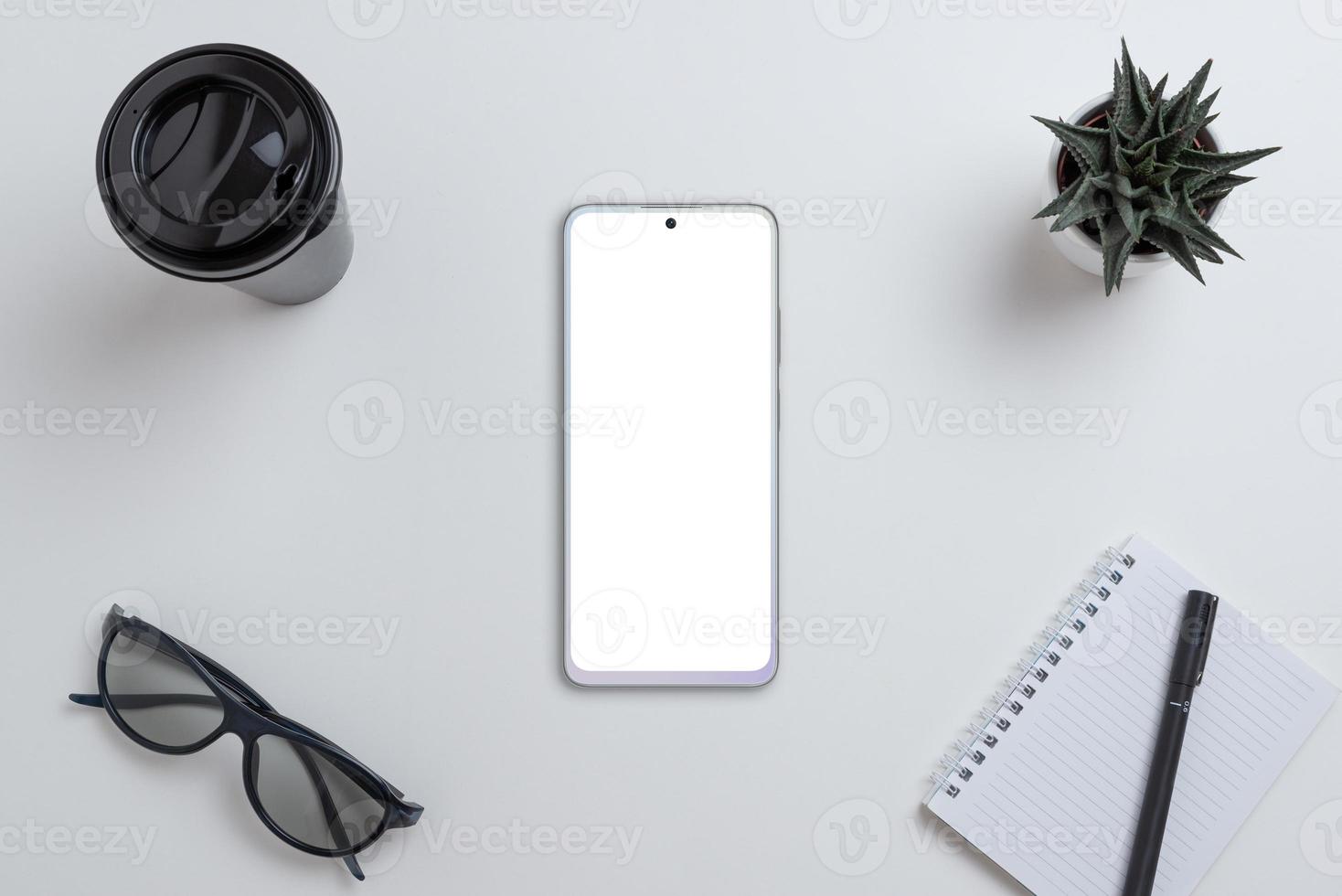 Gray phone mockup on work desk. Isolated screen for app design presentation. Top view, flat lay composition with coffee mug, glasses, pad, pen and plant photo