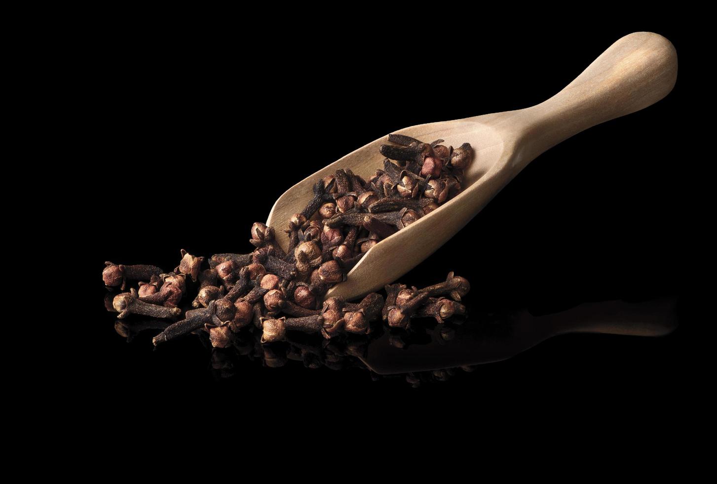 dried cloves in the wooden spoon, isolated on black  background photo