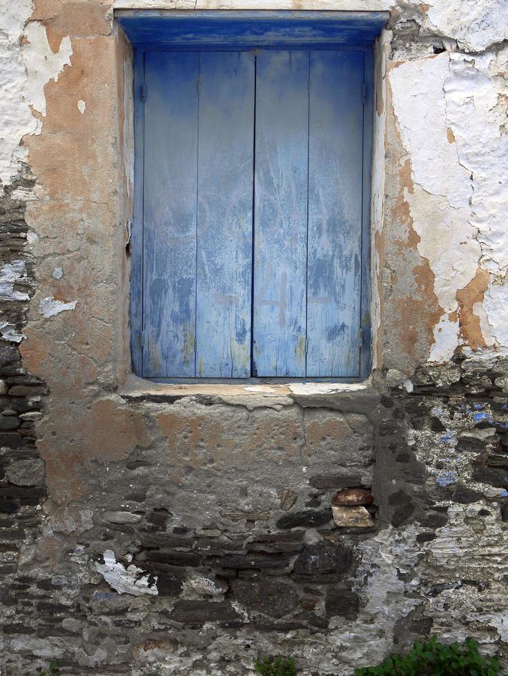 Ventanas de madera de color azul cerradas en la antigua pared de piedra pelada de yeso foto