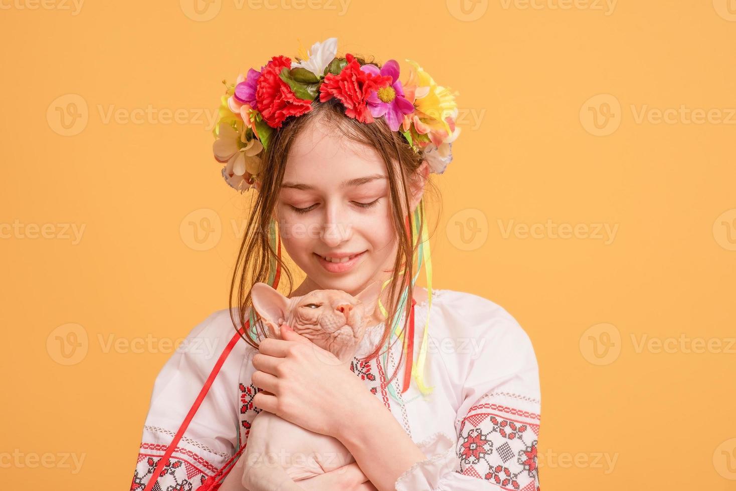 Teen girl with a wreath on her head and dressed in an embroidered shirt with a cat in her arms. Pet. photo