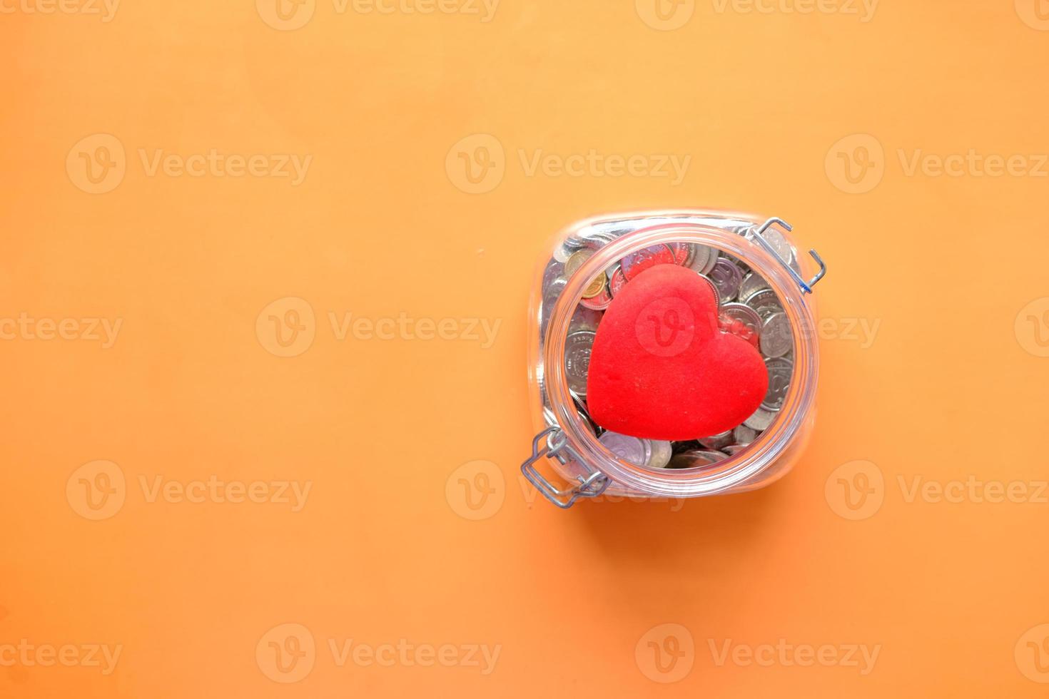 flat composition of Red heart and coins in a jar on orange background photo