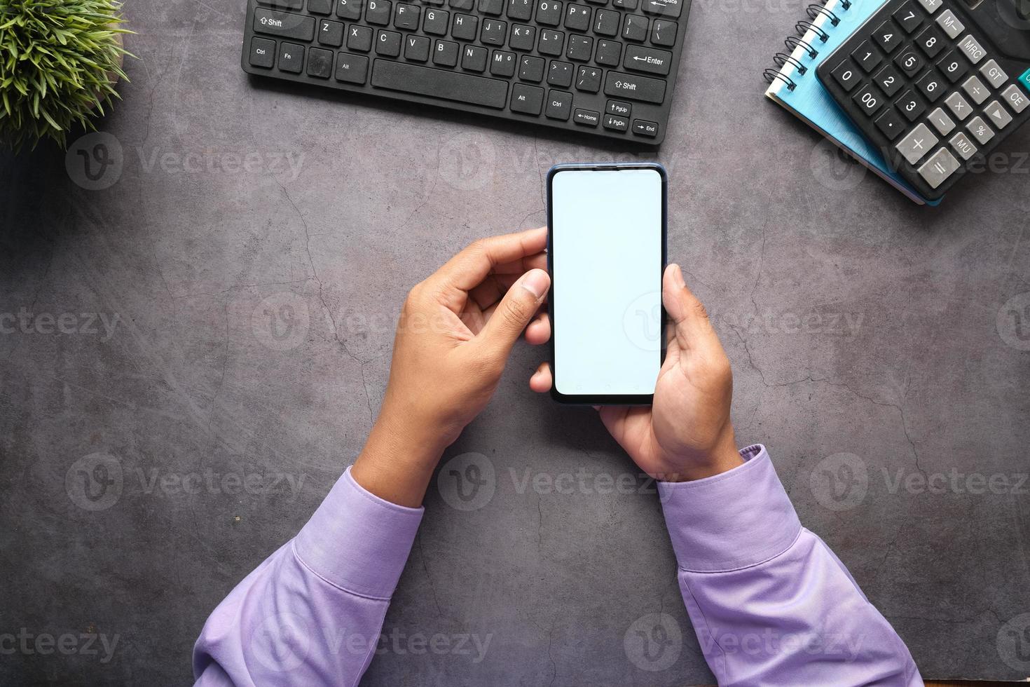 Top view of man hand holding smart phone with empty screen on office desk photo