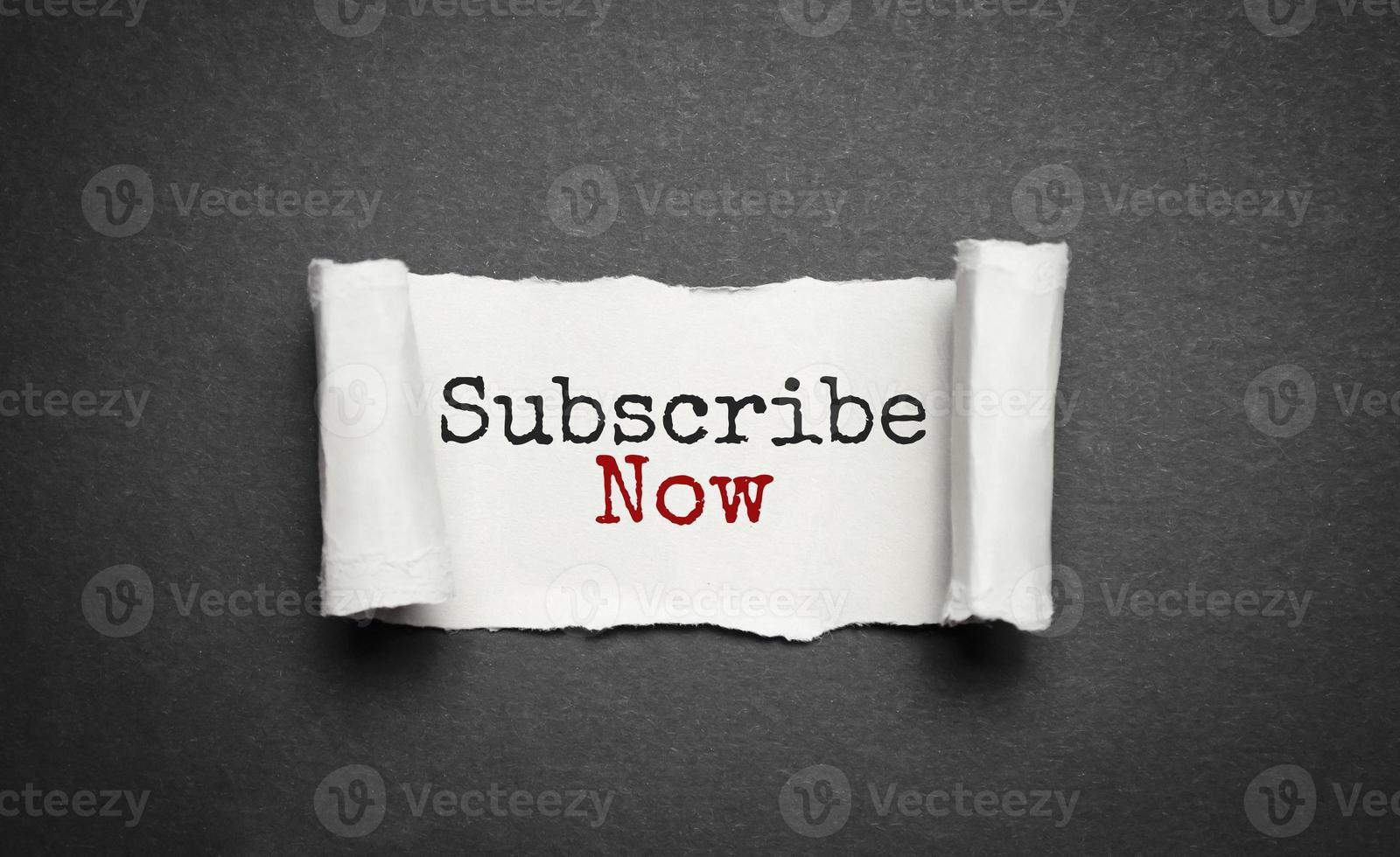 Text SUBSCRIBE NOW appearing behind torn brown paper. Top view. photo