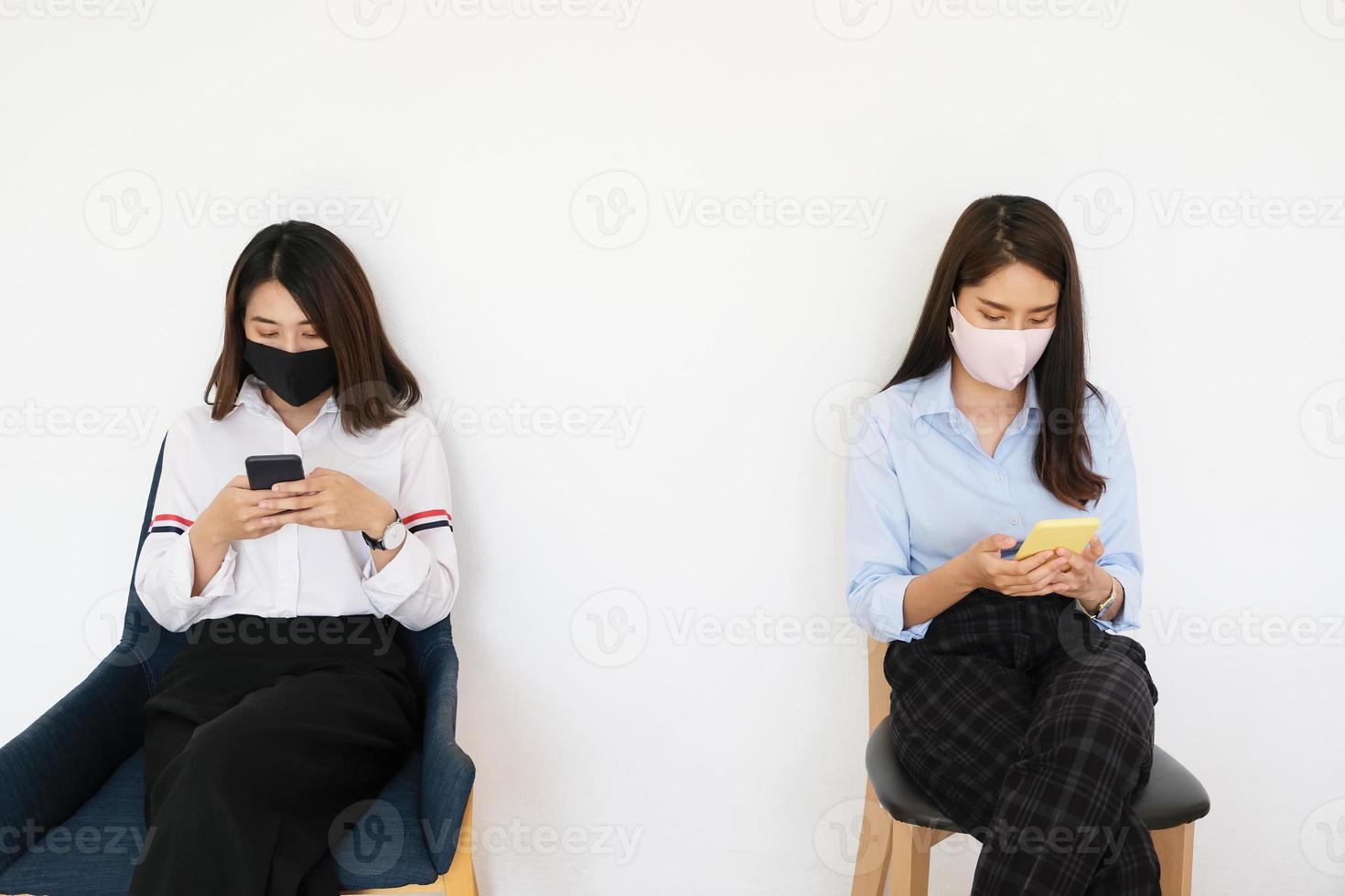 social distancing concept, Two women wearing masks and distancing while sitting on mobile phones following coronavirus social trend. photo