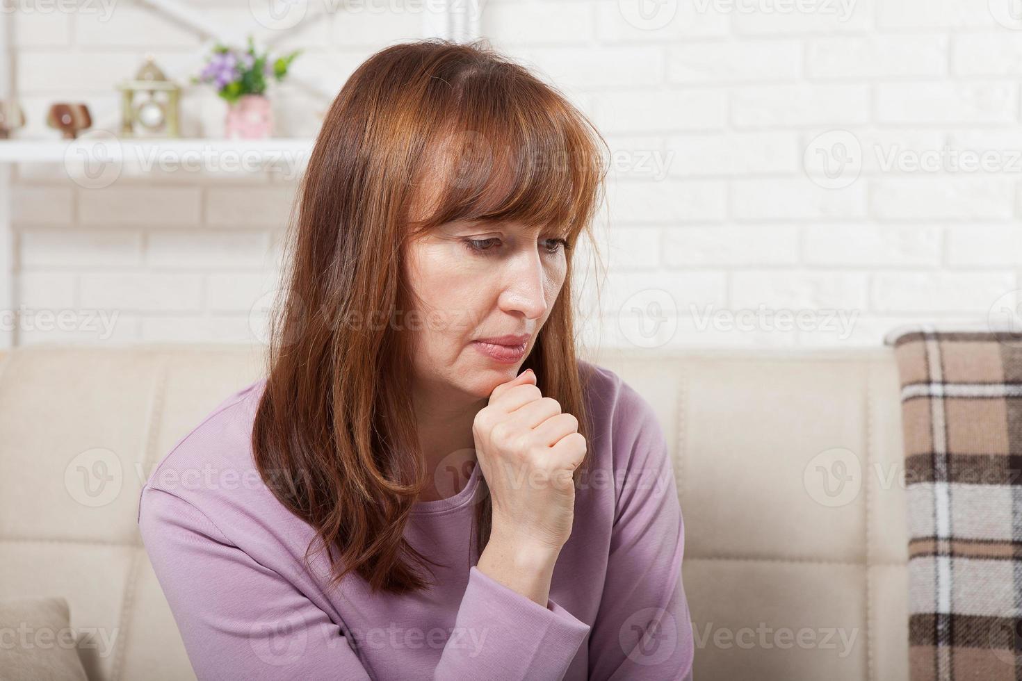 Sad middle age woman sitting on a sofa in the living room. Menopause photo