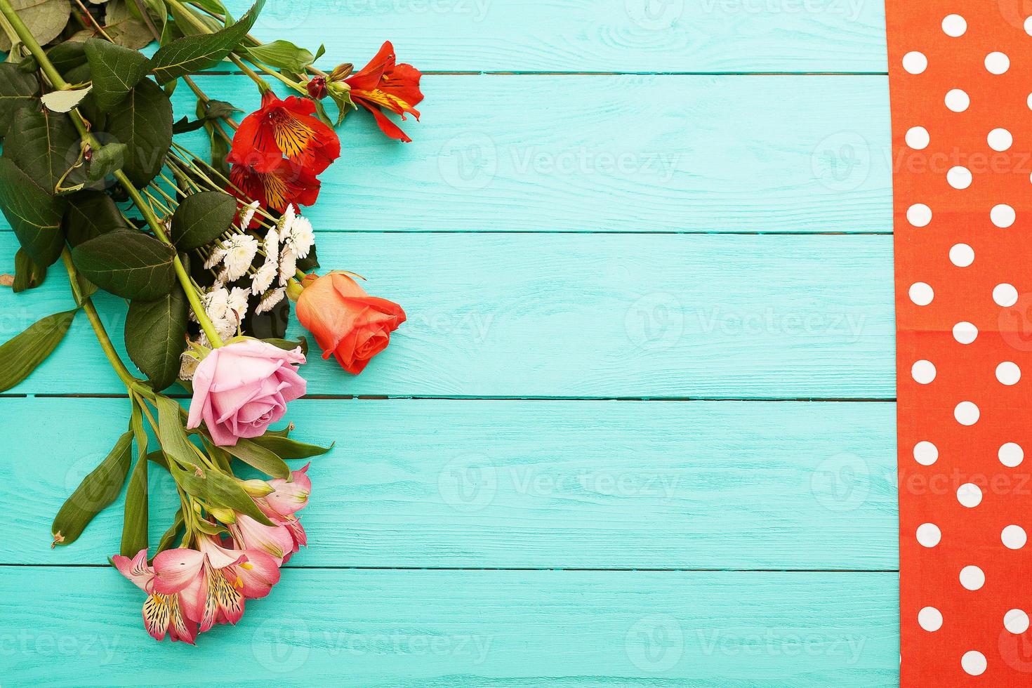 Frame of flowers and tablecloth in polka dots on blue wooden background. Top view and selective focus. Copy space photo