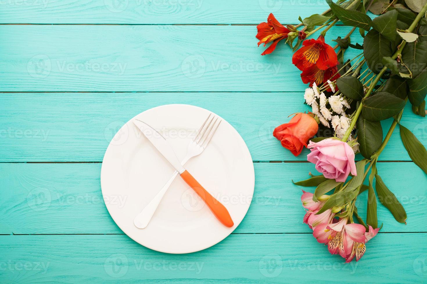 cena festiva con cubiertos, cuchillo, tenedor, plato y rosas sobre fondo de madera azul. vista superior. Bosquejo. flores copie el espacio foto